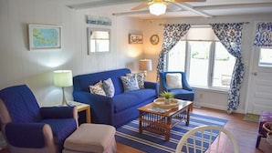 A cozy living room with a blue sofa, a matching armchair, a wooden coffee table, and a dining table with chairs. - Three bedroom duplex less than 500 ft to the shared/private beach (West Dennis)