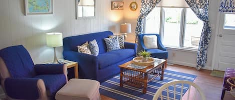 A cozy living room with a blue sofa, a matching armchair, a wooden coffee table, and a dining table with chairs.
