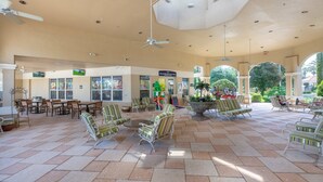 A spacious indoor area with tiled flooring, multiple seating areas with striped chairs, ceiling fans, and a large arched window allowing natural light.