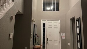 A hallway with a staircase, a chandelier, a door, and a mirror.