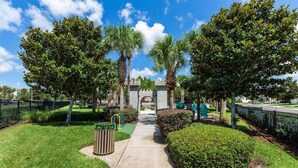A pathway leading to a gated entrance with a stone archway, surrounded by lush greenery and palm trees. - Renovated Jan 2026 5BR luxury villa in Grand Windsor Hills, 5-Star gated resort (Kissimmee)