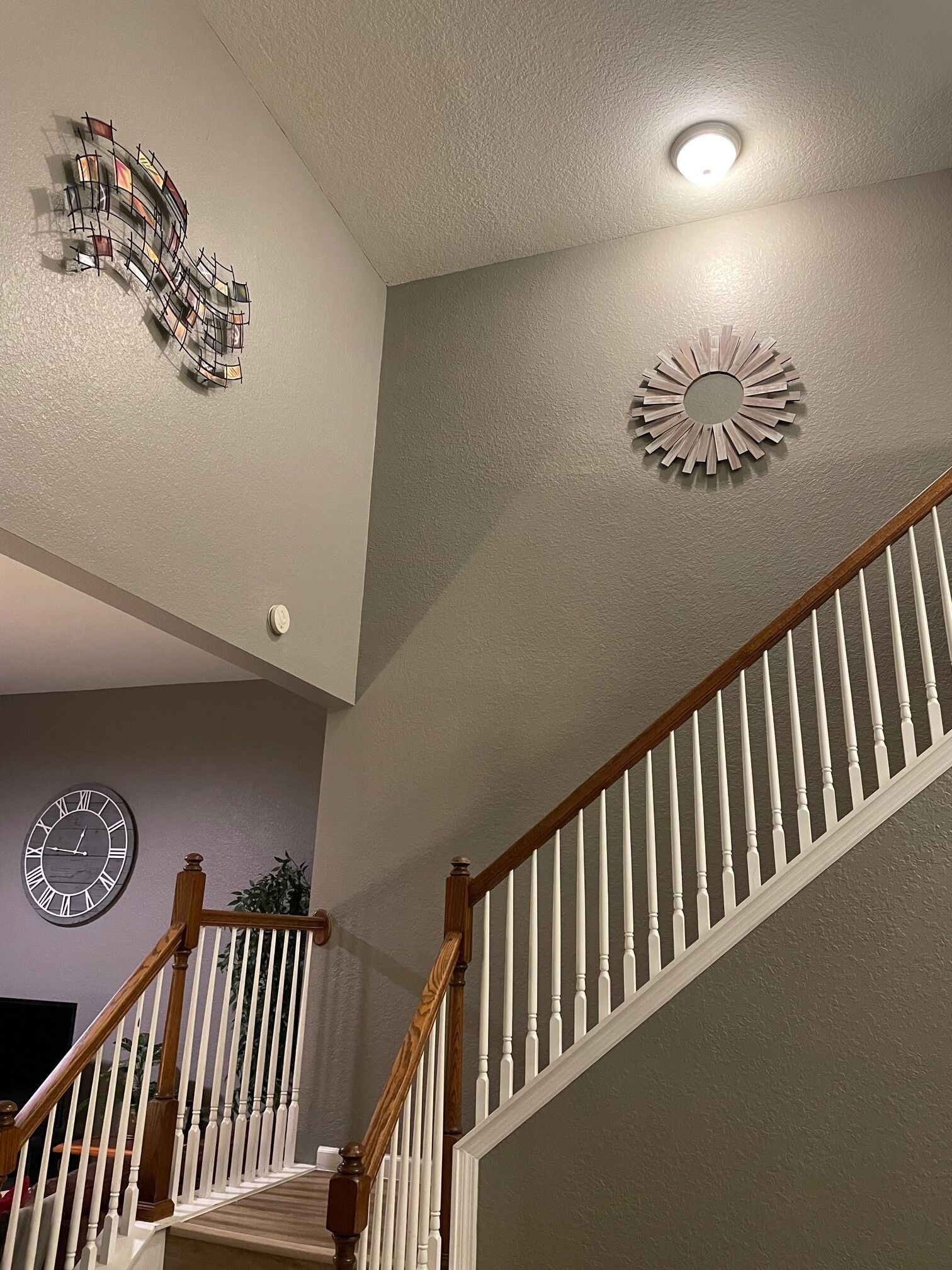 A staircase with white balusters and wooden handrails, a decorative wall clock, and a ceiling light fixture.