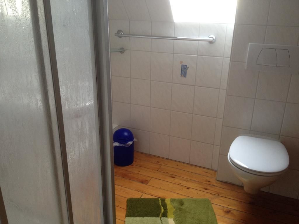 Um banheiro pequeno com piso de madeira, vaso sanitário branco e lixeira azul.