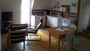 Angolo cottura funzionale con microonde, piano cottura e lavello. C'è un tavolo da pranzo con sedie, una poltrona a dondolo e una televisione nell'angolo.