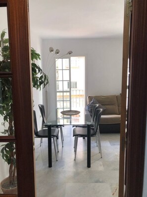 A dining area with a glass table and chairs, a sofa, and a potted plant.
