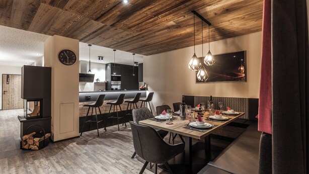 Un comedor moderno con techo de madera, un reloj grande y una mesa de comedor preparada para seis comensales.