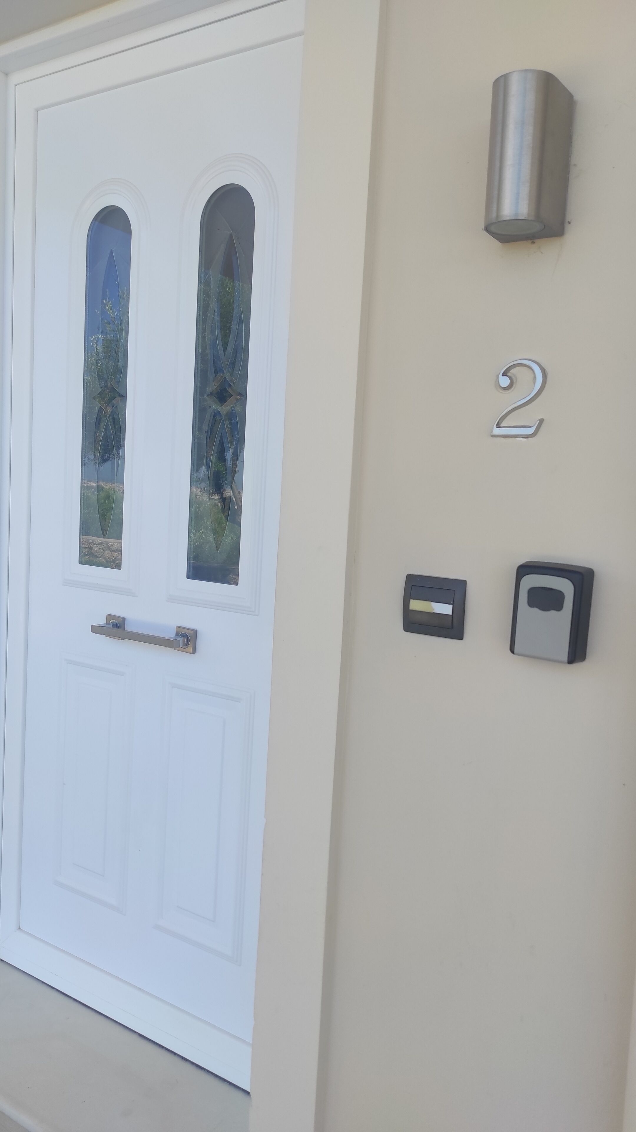 Une porte blanche ornée de deux fenêtres en arc de cercle, une boîte aux lettres et le numéro de la maison, « 2 », peint sur le mur.