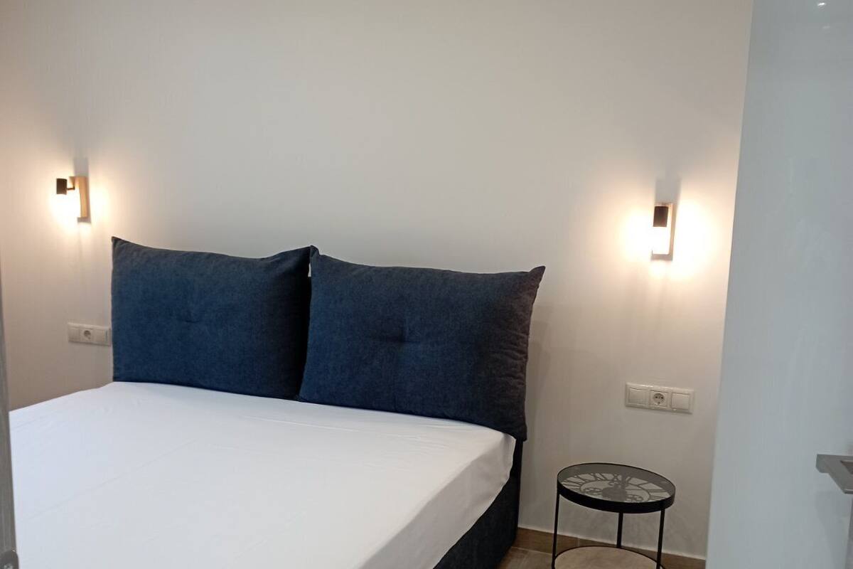 A bedroom with a bed, two pillows, a small round table, and wall-mounted lights.