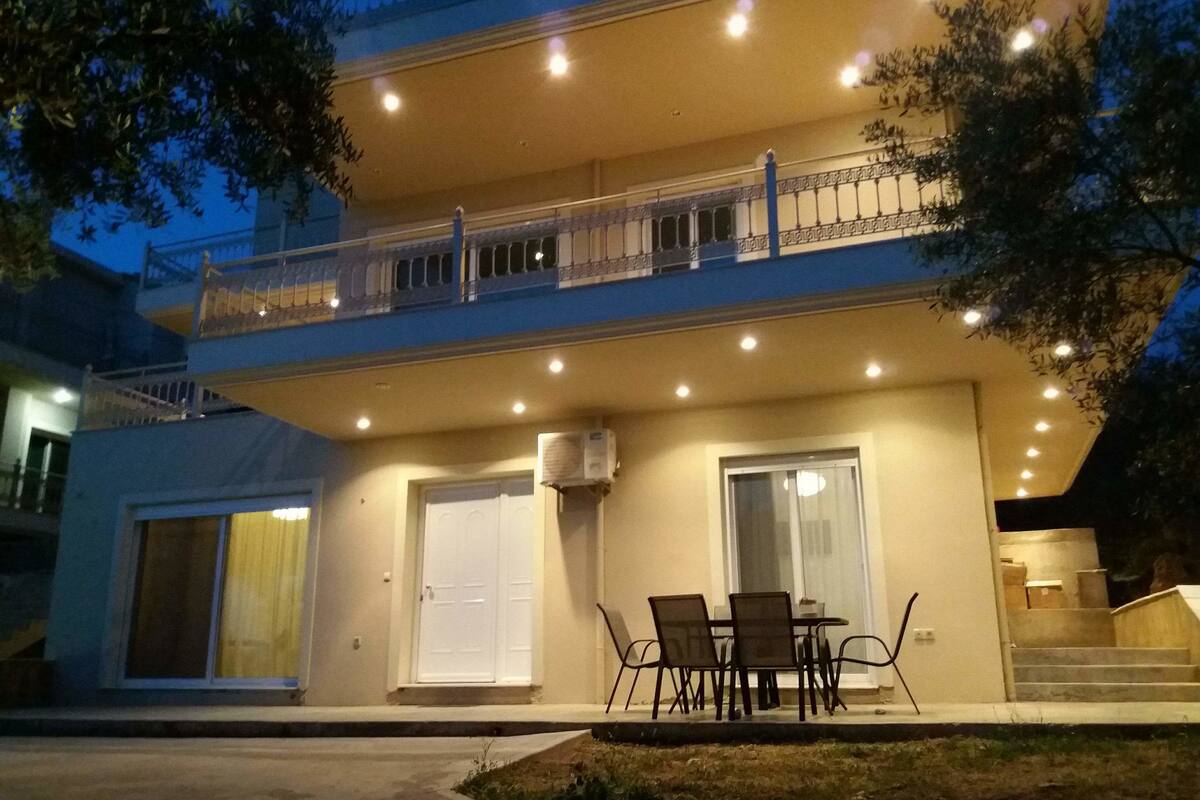 A two-story building with a balcony, a dining area with chairs and a table, and a staircase leading to an upper level.