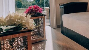 A bedroom with a bed, a table with flowers, and a view of greenery through a glass door. - Agriomata Vergas Apartments (Kalamata)