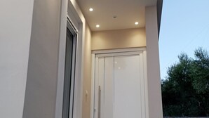 A modern building entrance with a white door, a window, and a stone wall. - Agriomata Vergas Apartments (Kalamata)