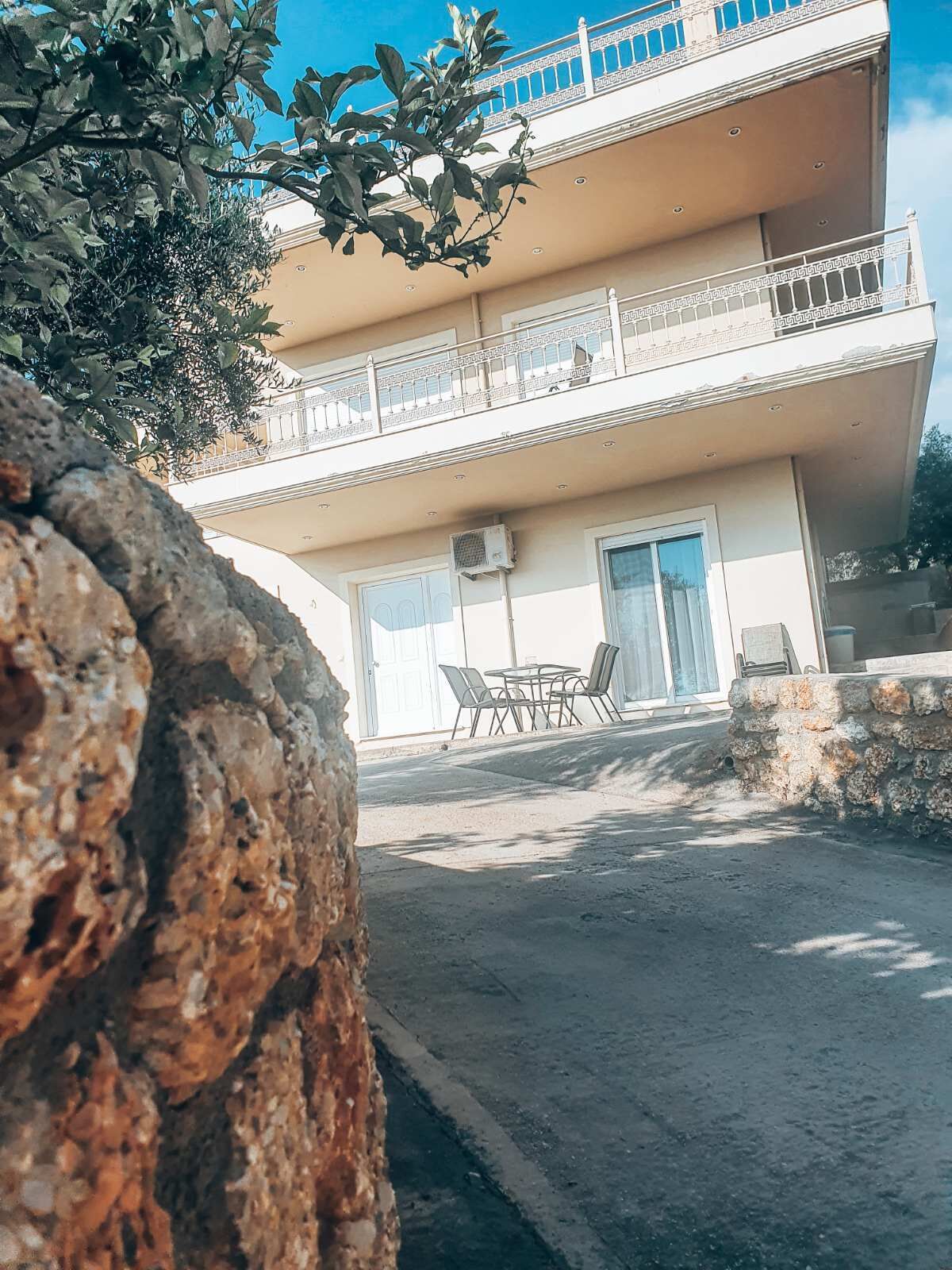 Un edificio de dos plantas con balcón, asientos exteriores y un muro de piedra.