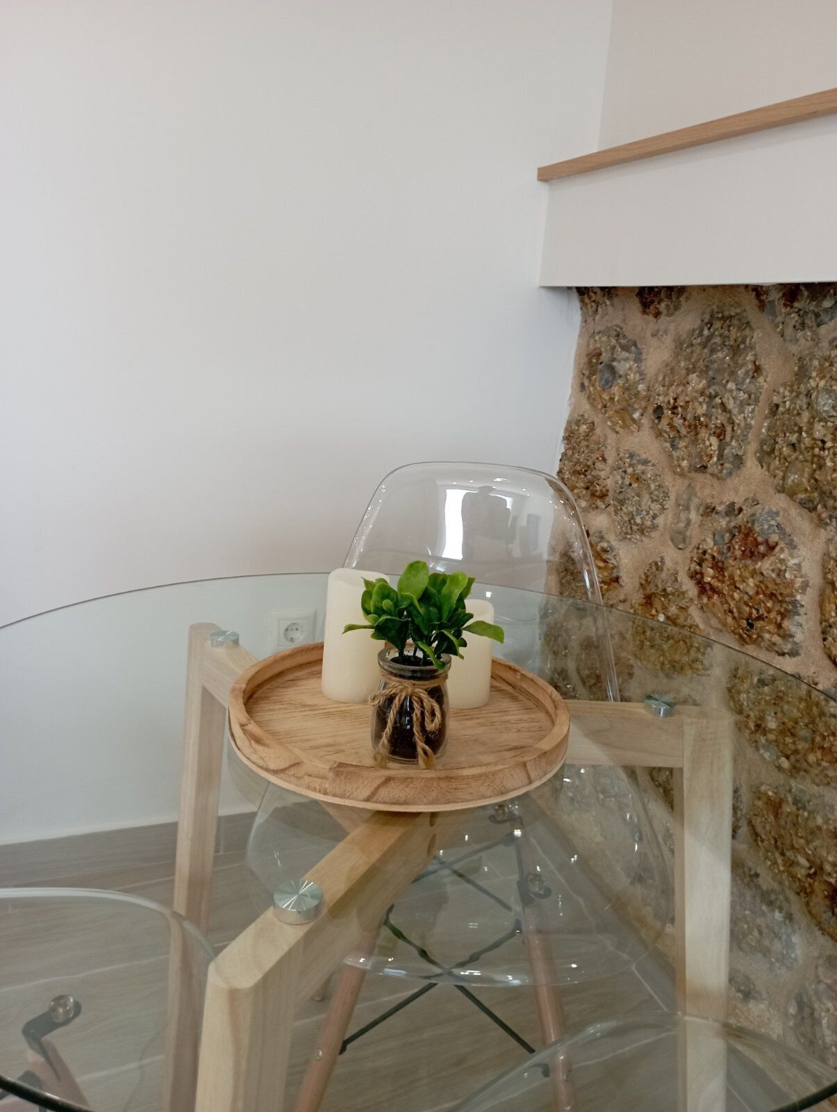 A glass table with a wooden tray, a small potted plant, and two candles.