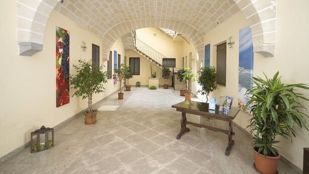 Un hall d’entrée spacieux, doté d’un haut plafond en arc de cercle, de plantes en pot, d’un escalier et d’une table sur laquelle sont posés des magazines.