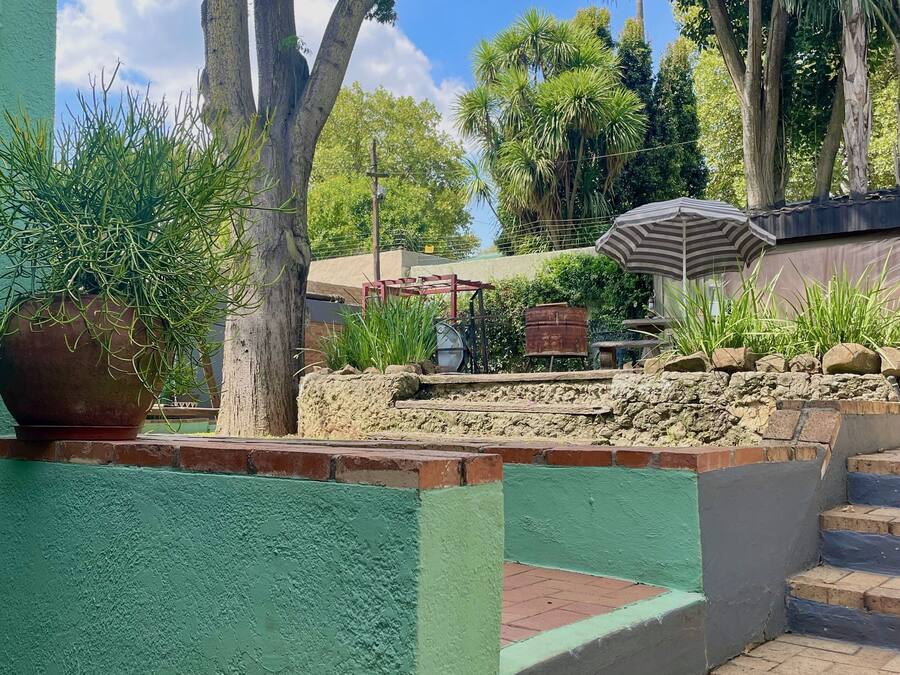 Un patio con un muro verde, un sendero de ladrillo, un banco de metal y un paraguas grande.