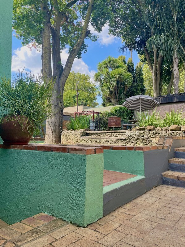 A courtyard with a green wall, a brick pathway, a metal bench, and a large umbrella. - Timebridge Mansion (Johannesburg)