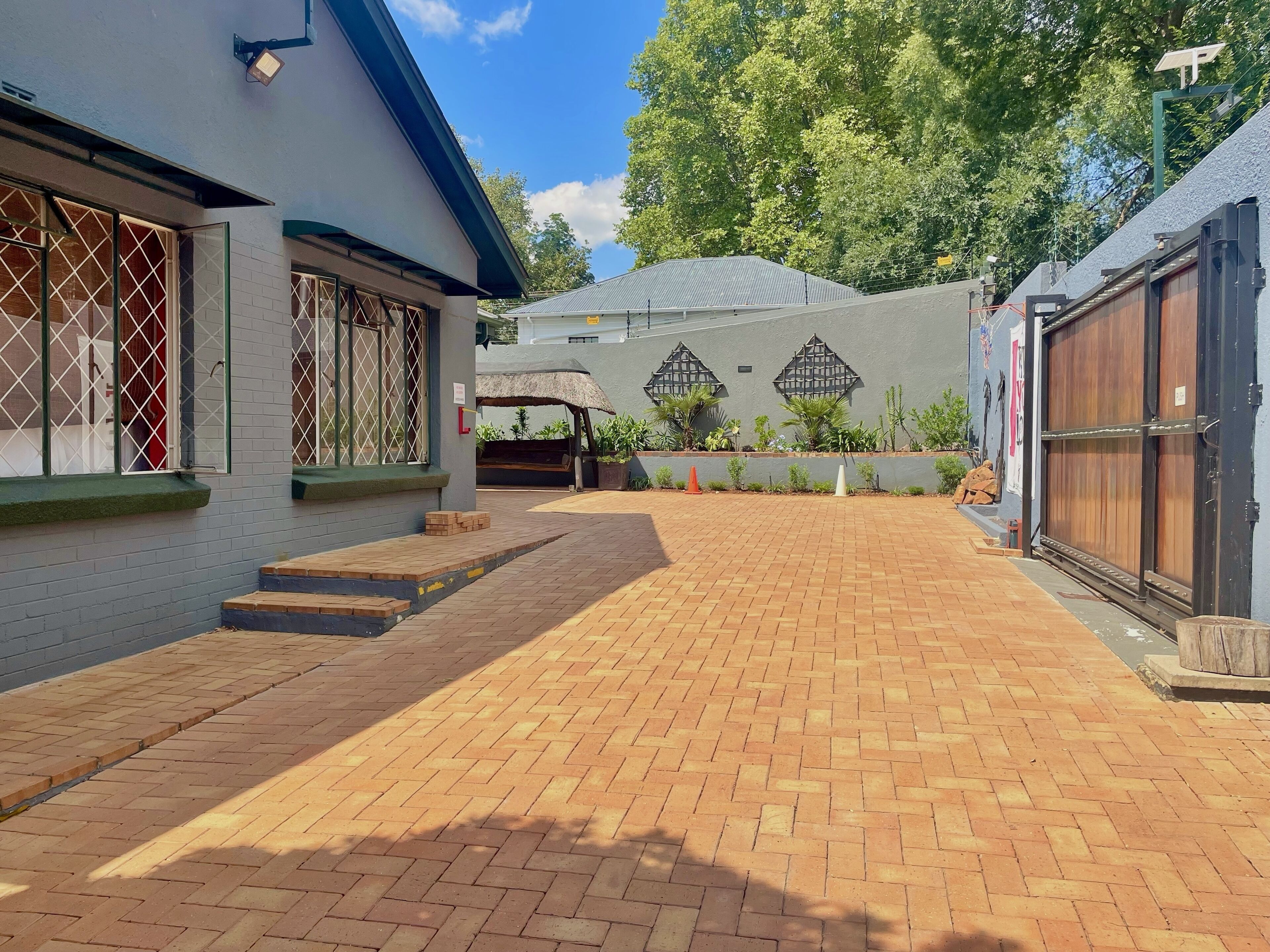 A courtyard with a brick pathway, a covered seating area, and a building with a metal gate.