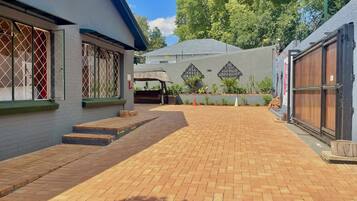 A courtyard with a brick pathway, a covered seating area, and a building with a metal gate.