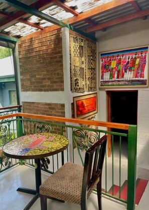 A balcony with a tiled table and chair, a brick wall, a patterned wall decoration, and a colorful mural. - Timebridge Mansion (Johannesburg)