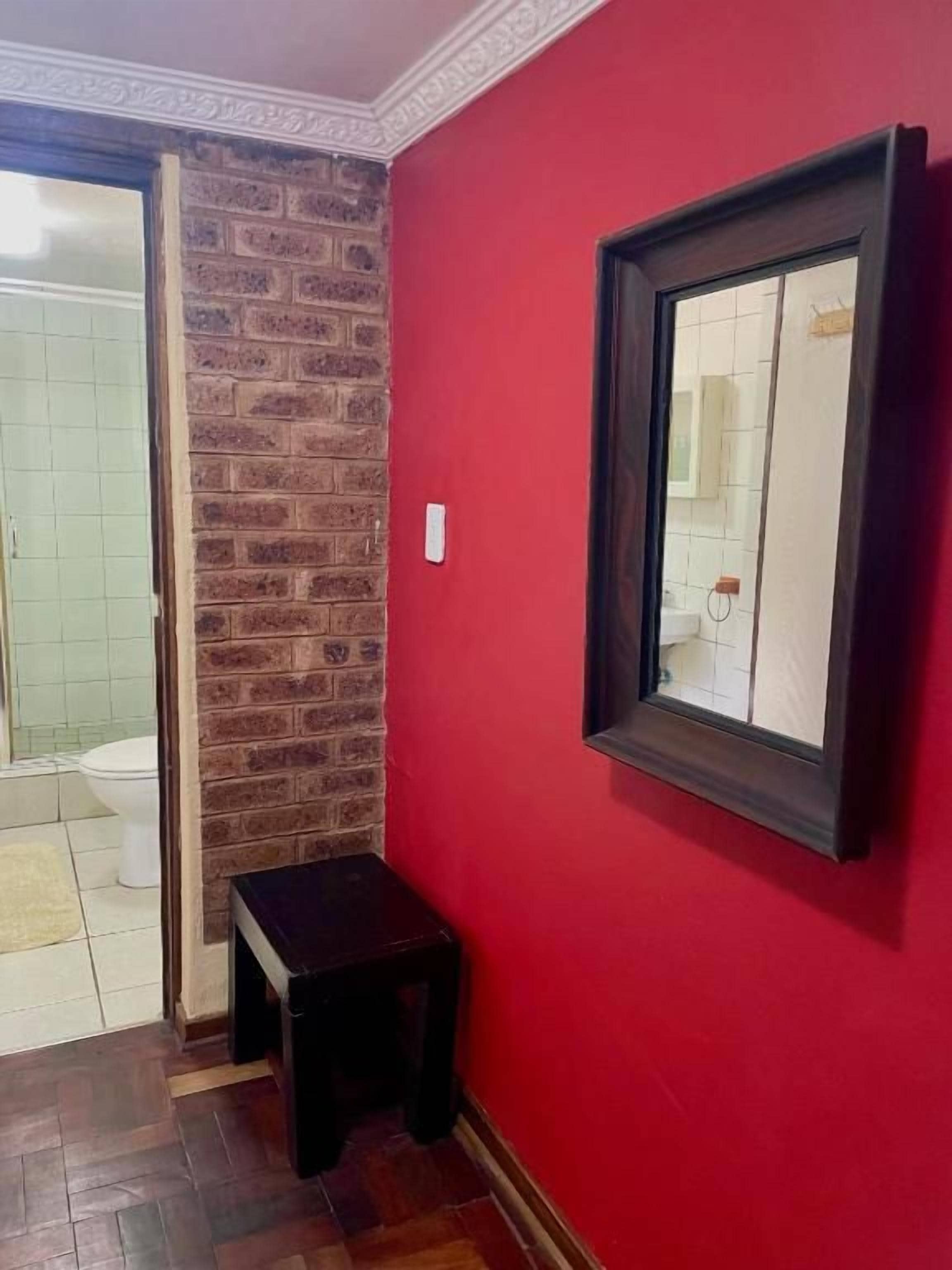A bathroom with a red wall, a wooden bench, and a mirror.