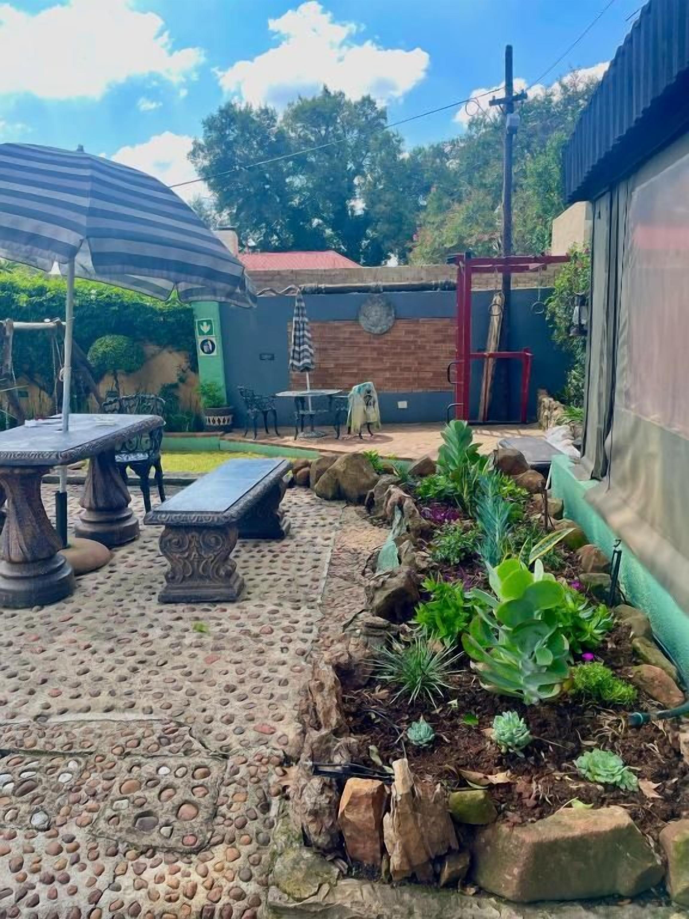 An outdoor patio area with a stone floor, a table, chairs, and a bench. There are plants and a small garden bed with various succulents.