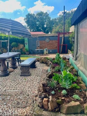 An outdoor patio area with a stone floor, a table, chairs, and a bench. There are plants and a small garden bed with various succulents. - Timebridge Mansion (Johannesburg)