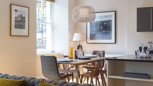 A modern living room with a dining area, featuring a sofa, chairs, a table, and a kitchen counter with appliances. - JOIVY 5-star Luxurious George Street Apartment (Edinburgh)