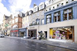 A street view with a row of shops, including a cafe and a store with a bright display window. - JOIVY 5-star Luxurious George Street Apartment (Edinburgh)