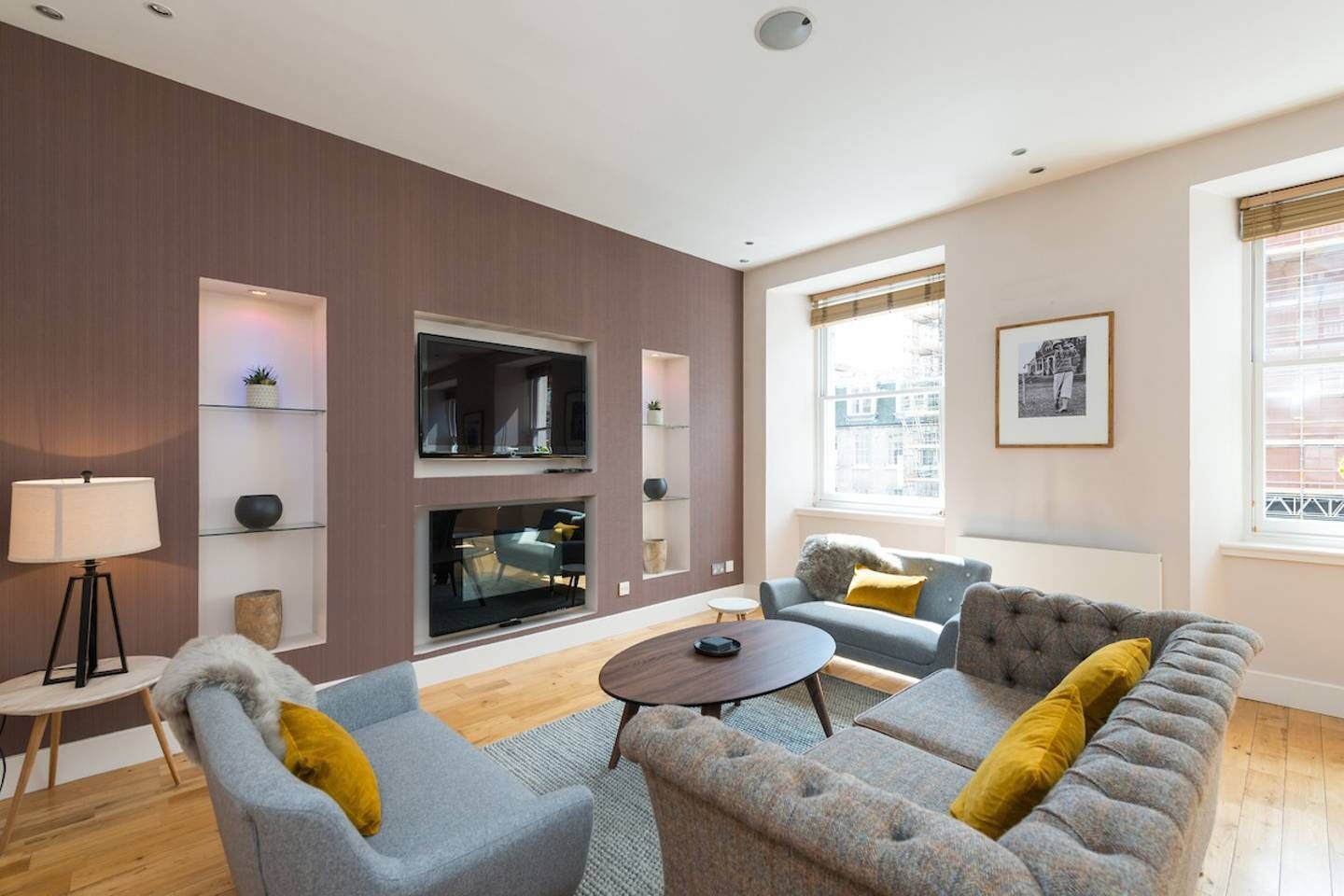 A modern living room with a sofa set, a coffee table, and a floor lamp. There are built-in shelves and a large window with a view of buildings.
