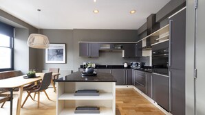 A modern kitchen with grey cabinets, a central island, and a dining area with a wooden table and chairs. - JOIVY 5-star Luxurious George Street Apartment (Edinburgh)