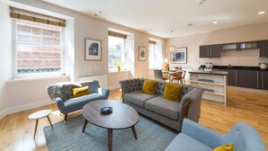 A modern living room with a sofa, armchairs, and a coffee table. There is a kitchen area with cabinets and a dining table. - JOIVY 5-star Luxurious George Street Apartment (Edinburgh)
