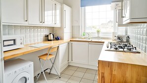 A modern kitchen with white cabinets, a wooden countertop, a gas stove, a microwave, and a washing machine. - JOIVY Bright Royal Mile Apartment (Edinburgh)