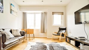 A modern living room with a leather sofa, a rocking chair, a flat-screen TV, and a large cowhide rug. - JOIVY Bright Royal Mile Apartment (Edinburgh)