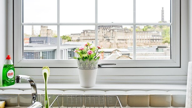 A window with a view of buildings and a potted plant with flowers on a windowsill. - JOIVY Bright Royal Mile Apartment (Edinburgh)