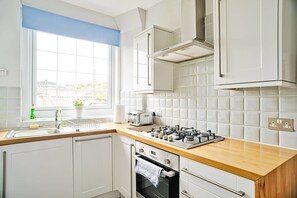 A modern kitchen with white cabinets, a wooden countertop, a gas stove, a built-in oven, and a window with a view of the city. - JOIVY Bright Royal Mile Apartment (Edinburgh)