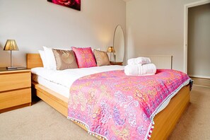 A neatly made bed with a pink patterned bedspread, white pillows, and a rolled-up towel on the side. - JOIVY Bright Royal Mile Apartment (Edinburgh)