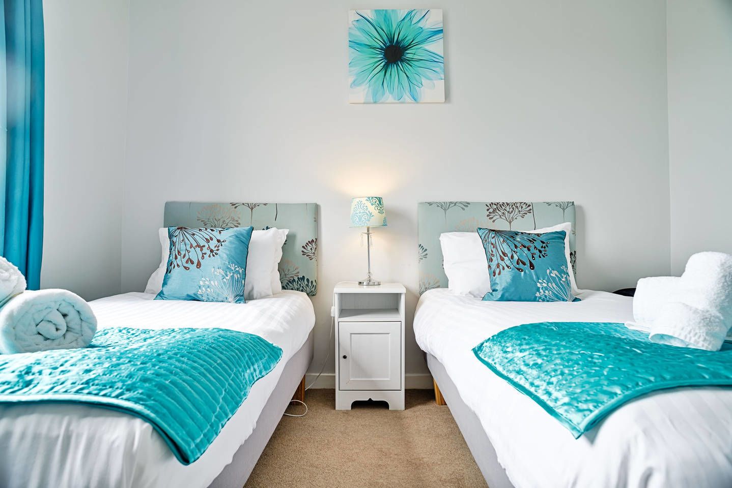 Une chambre d’hôtel avec deux lits, chacun agrémenté d’une parure de lit assortie aux couleurs bleu et blanc, une petite table de chevet avec une lampe, et une œuvre d’art murale au-dessus des lits.
