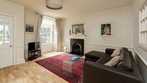A living room with a fireplace, a sofa, a TV, and a bookshelf. - JOIVY New Town Boutique Apartment on India Street (Edinburgh)
