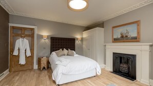 A bedroom with a large bed, a fireplace, a door with a robe hanging, and a painting on the wall. - JOIVY New Town Boutique Apartment on India Street (Edinburgh)