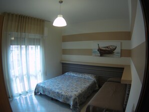 Un dormitorio con una cama, una mesita de noche, una lámpara colgante, una ventana con cortinas y un cuadro de un barco colgado en la pared.