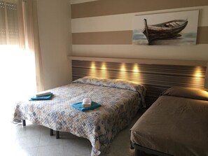 Ein Hotelzimmer mit Bett, Nachttisch, einem Kopfteil mit Beleuchtung, einem Bild an der Wand und einem Fenster mit Vorhängen.
