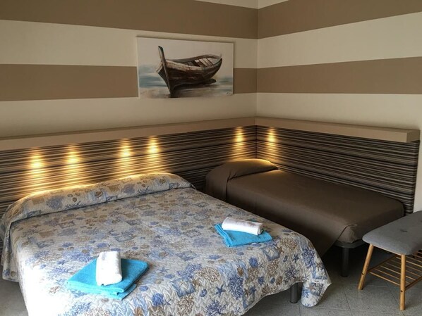 Habitación de hotel con pared a rayas, cama con ropa de cama floral, un banco y una mesita.