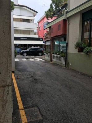 Vista de la calle con un coche negro estacionado en la banquina, edificios con locales comerciales y un paso de peatones.