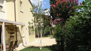Une maison dotée d’un patio couvert, d’une petite pelouse et d’un arbre aux fleurs roses.