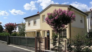 Un immeuble résidentiel de deux étages, doté d’une façade beige, d’une entrée sécurisée par un portail et d’un arbre aux fleurs roses devant.