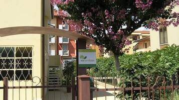 Ein verschlossenes Eingangstor mit einem Schild für Via Verde B&B, ein Gebäude mit Balkonen und einem blühenden Baum.