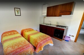 A compact room with two beds, a kitchenette, and a small bathroom.