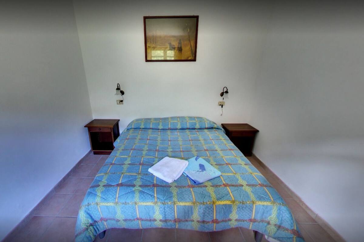 Un dormitorio con una cama, dos mesitas de noche, un cuadro colgado en la pared y dos lámparas de pared.