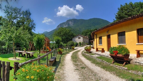 A rural village with stone buildings, a dirt path, wooden fences, and potted plants.