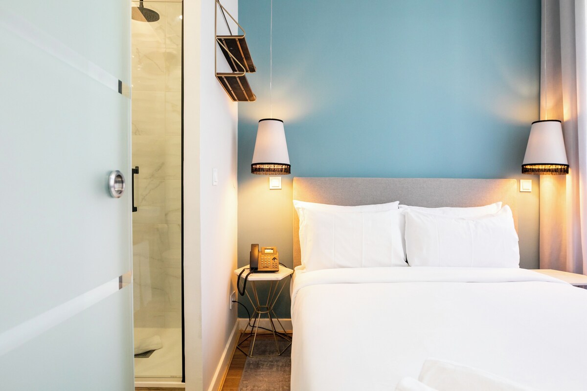 A hotel room with a bed, bedside lamps, a phone, and a shower area.